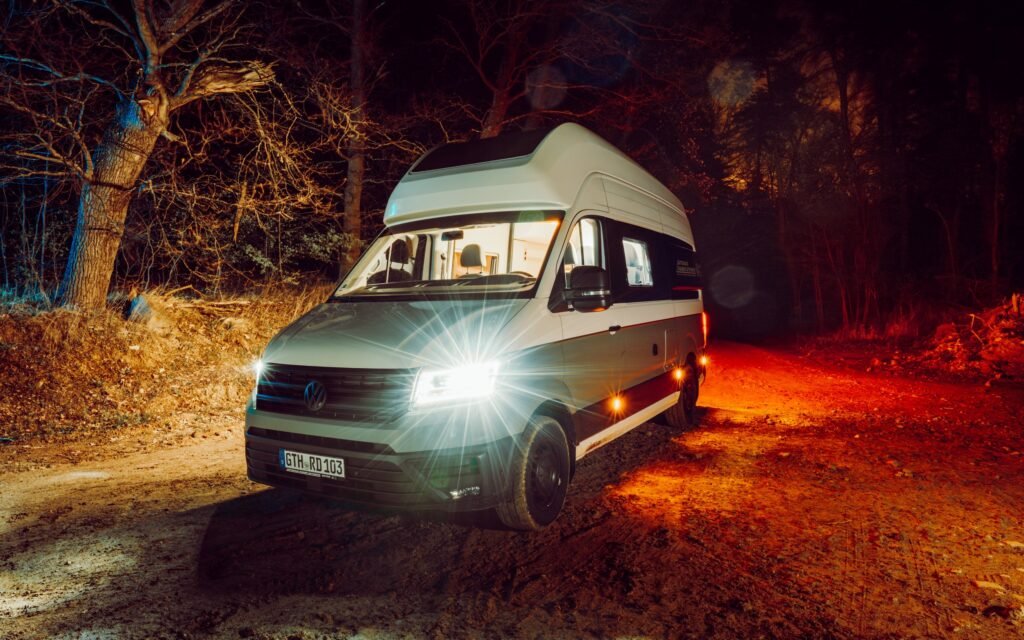 Camper mit geöffnetem Aufstelldach und Scheinwerfern bei Nacht