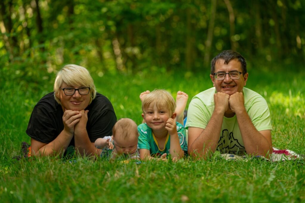 Familie liegt gemeinsam auf einer Wiese vor grünen Bäumen