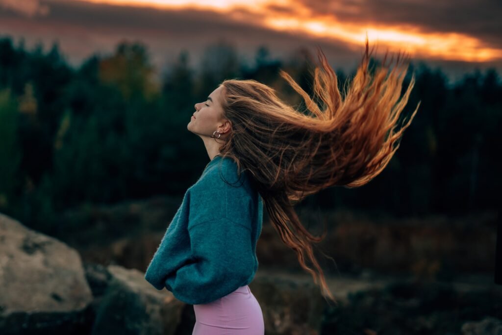 Frau mit wehenden Haaren vor einer Landschaft im Abendlicht