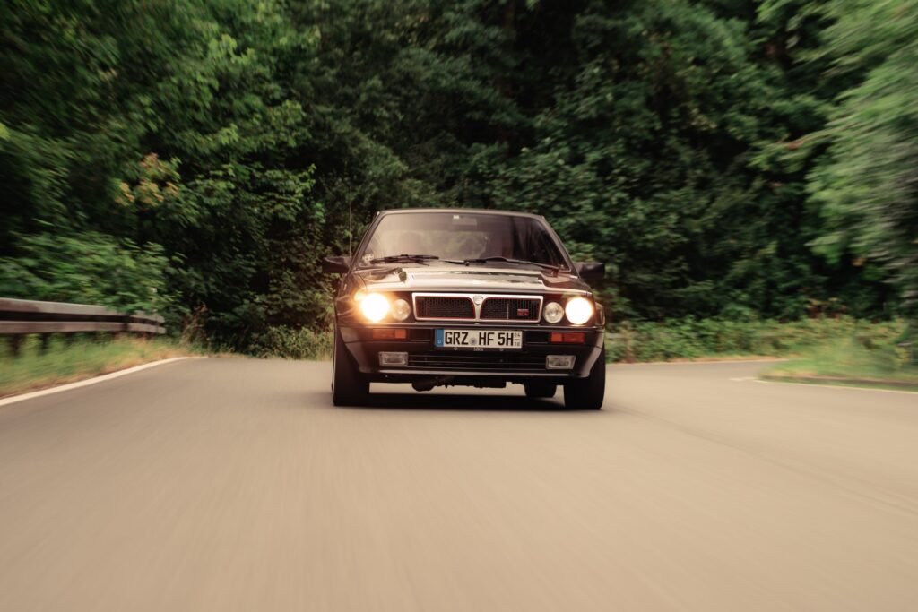 Schwarzer BMW mit eingeschalteten Scheinwerfern auf einer Waldstraße