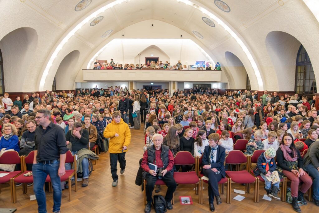 Publikum in einem hellen Saal mit gewölbter Decke