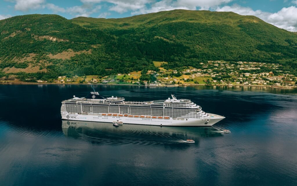 Kreuzfahrtschiff vor grünen Berghängen am Fjord