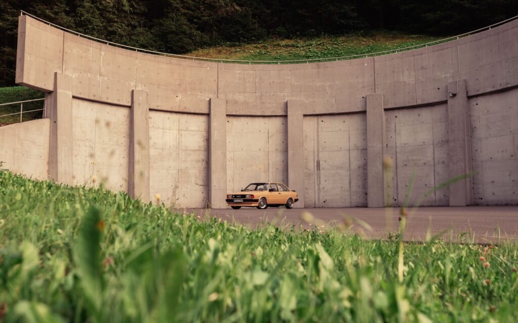 Heller Audi 80 vor hoher Betonwand mit Wiese im Vordergrund
